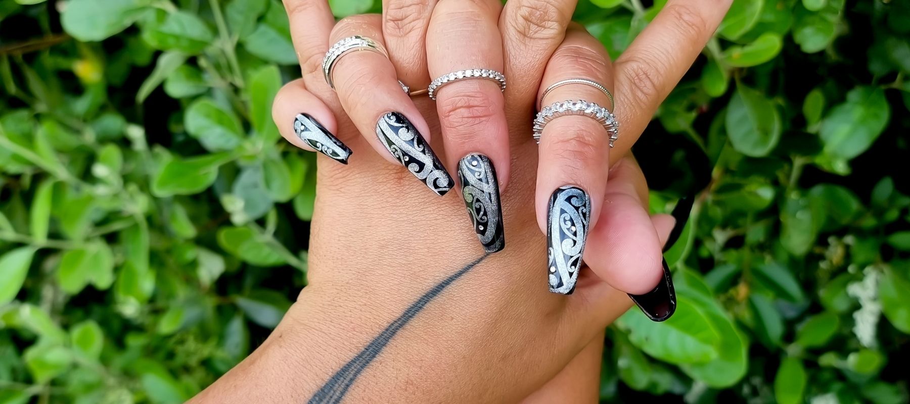 Black and silver Maori nails with Swarovski crystals with green bush in the background