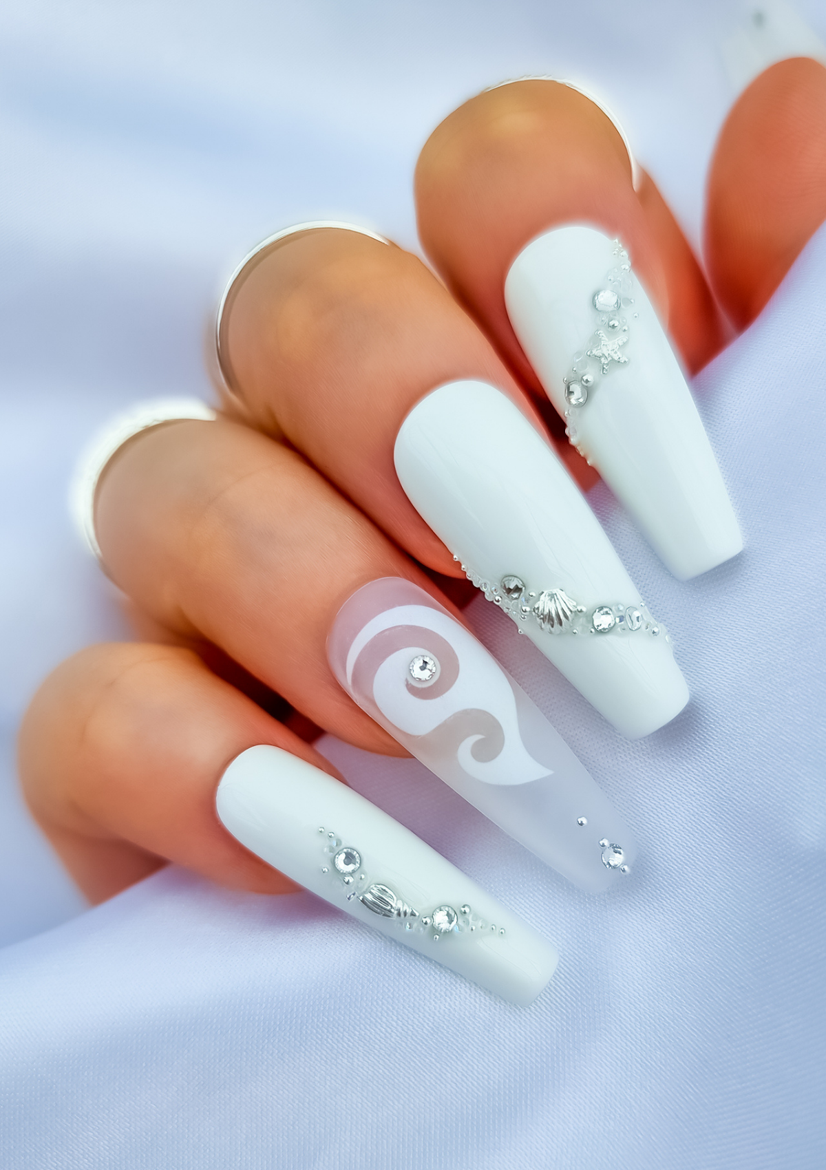 White nails with hei matau nail decal on ring finger and silver sea themed crystal design