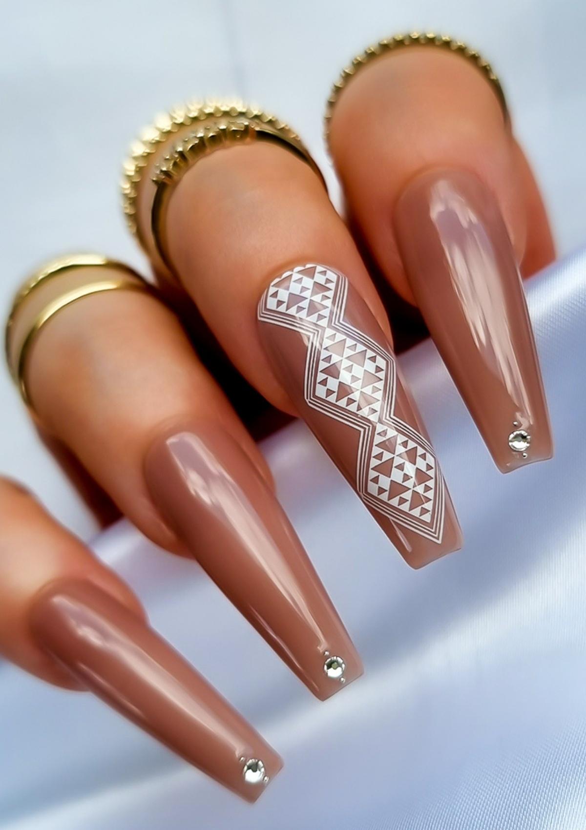 Long coffin shaped nails in light brown with white Maori nail art on the middle finger. Nail art design in Aonui pattern by Adrienne Whitewood.  