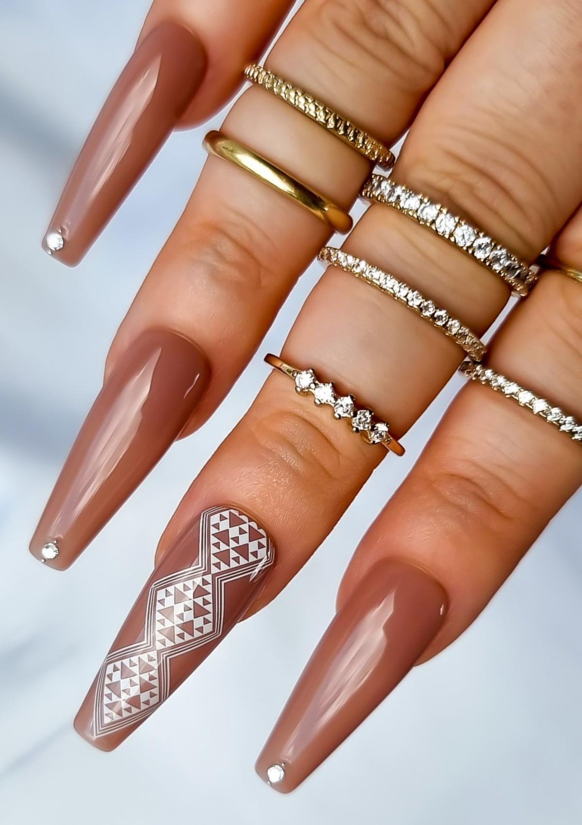 Long coffin shaped nails in light brown with white Maori nail art on the middle finger. Nail art design in Aonui pattern by Adrienne Whitewood.  