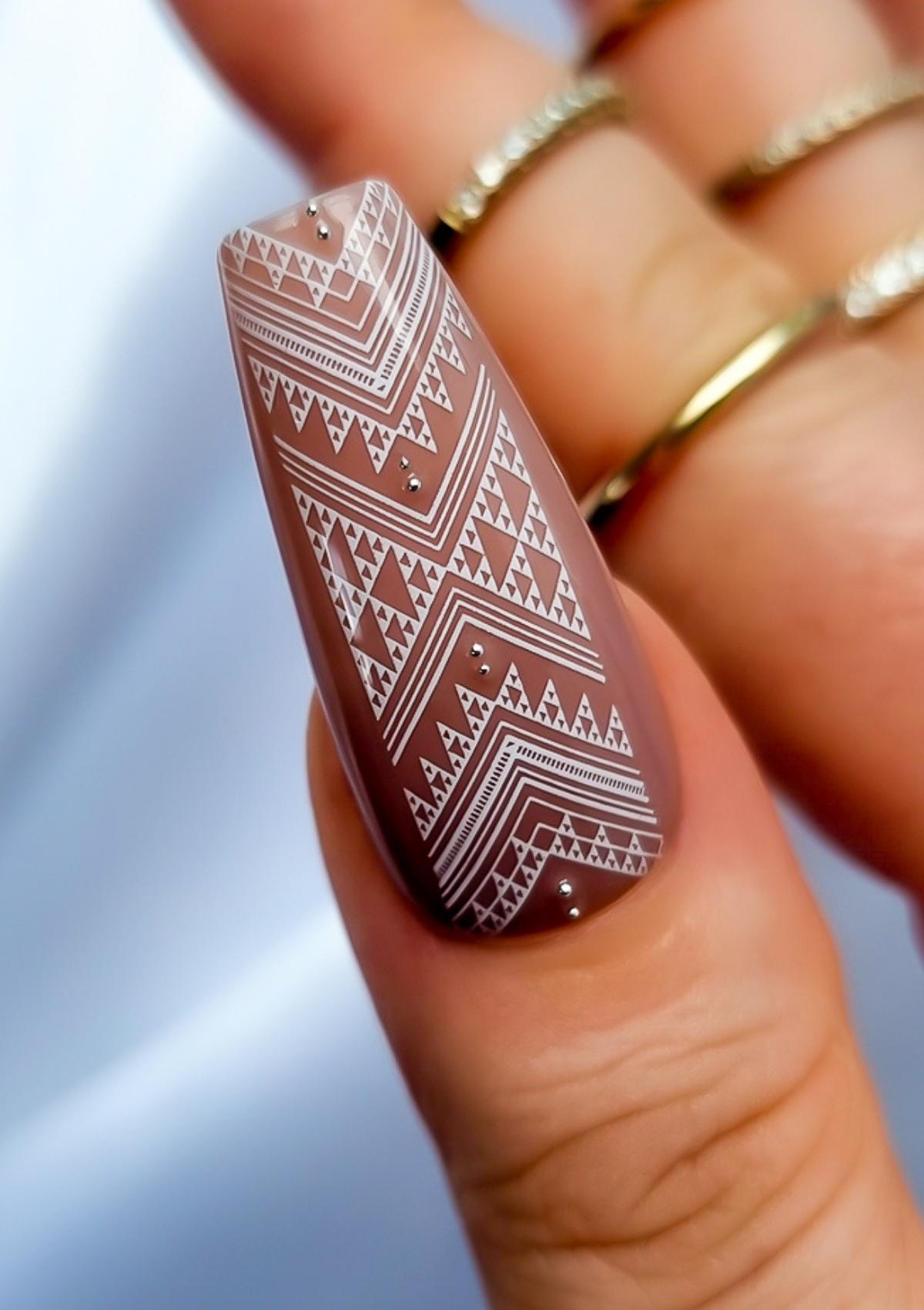 Long coffin shaped thumb nail in light brown with white Maori nail art. Nail art design in Taniko Hou pattern by Adrienne Whitewood.  