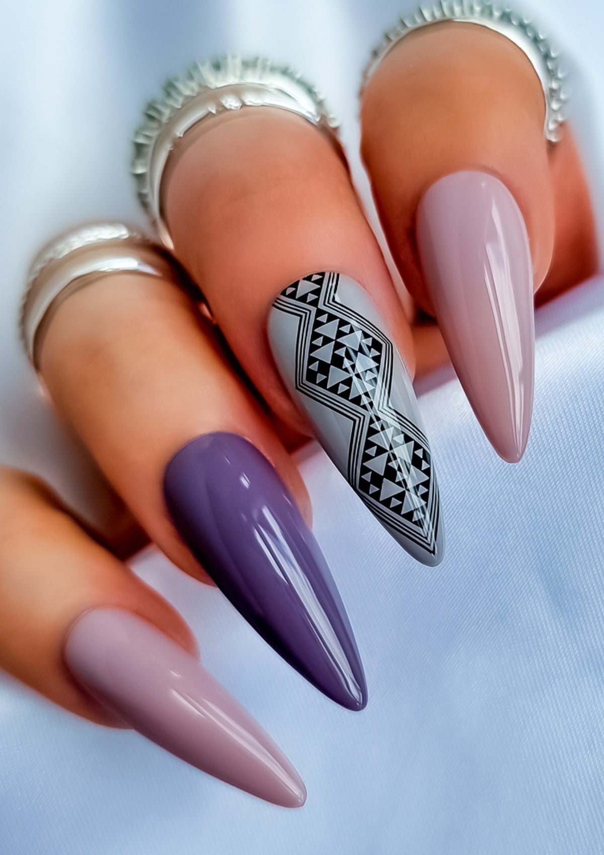 Long almond shaped nails in different shades of mauve and grey  with black Maori nail art on the middle finger. Nail art design in Aonui pattern by Adrienne Whitewood.  