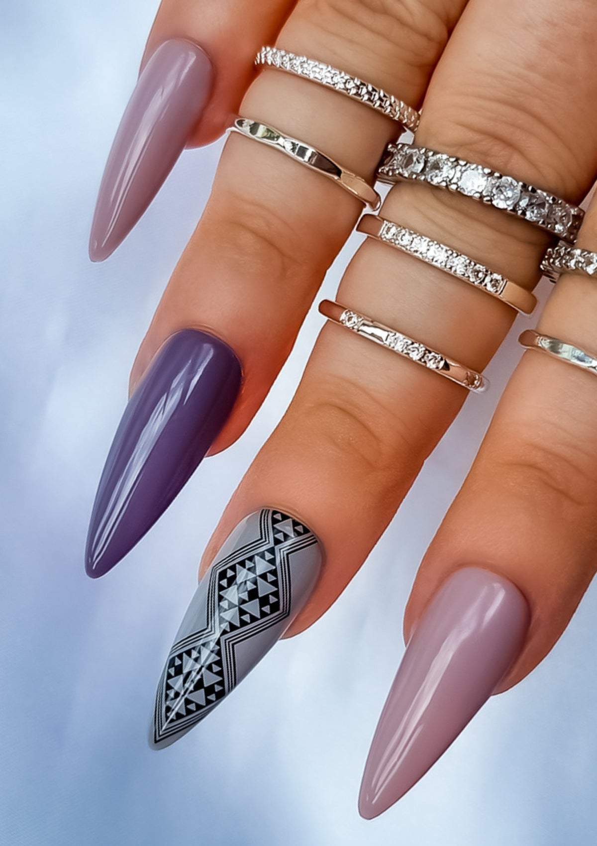 Long almond shaped nails in different shades of mauve and grey  with black Maori nail art on the middle finger. Nail art design in Aonui pattern by Adrienne Whitewood.  