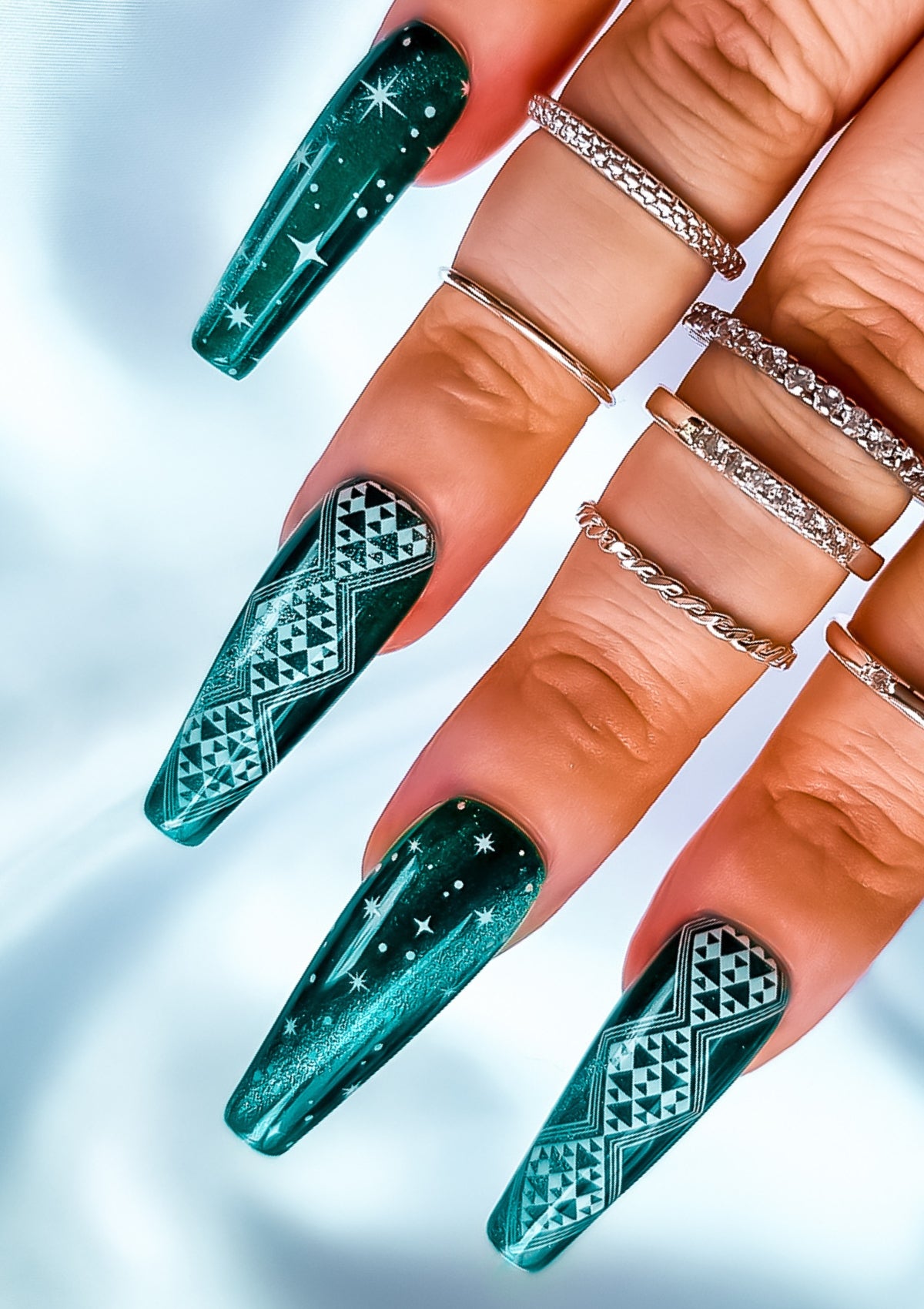 Long coffin shaped nails in emerald cat eye gel polish with white Maori nail art in Aonui design by Adrienne Whitewood on the index and ring fingers, and stars on the pinky and middle fingers.