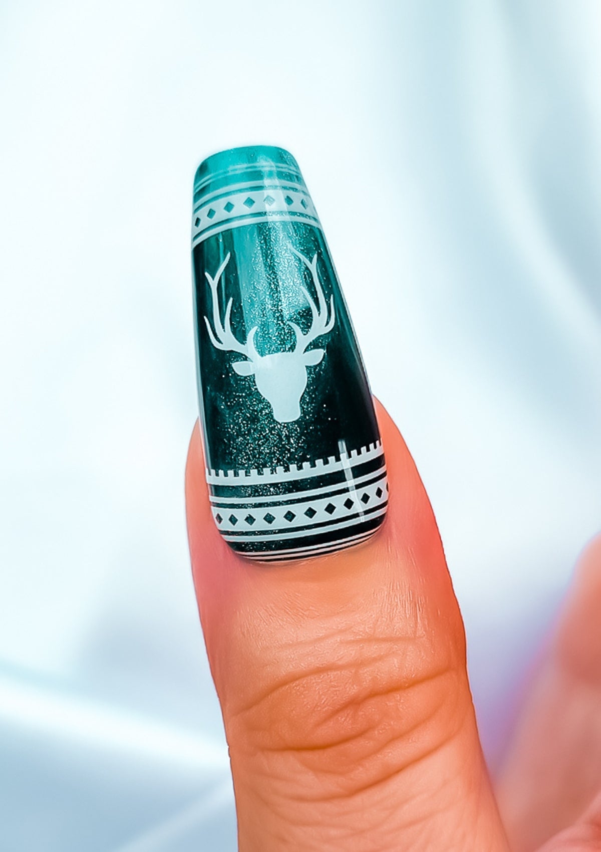 Long coffin shaped thumb nail in emerald cat eye gel polish with white reindeer head and Christmas patterns. 