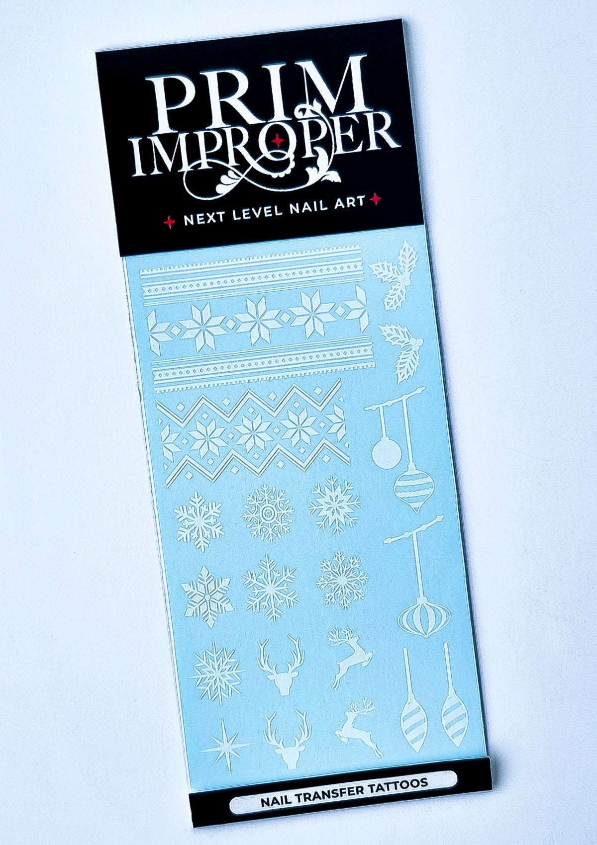 Sheet of white Christmas Nail Transfer Tattoos featuring Nordic sweater patterns, snowflakes, holly, reindeer, stars and Christmas baubles.